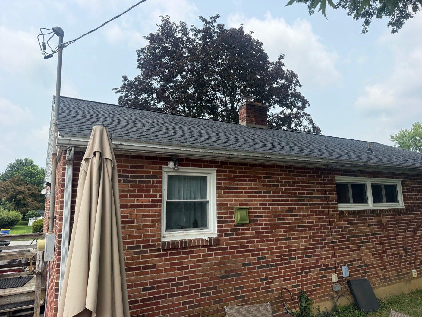 Rear of a brick ranch home with a new dark architectural shingle roof and a patio