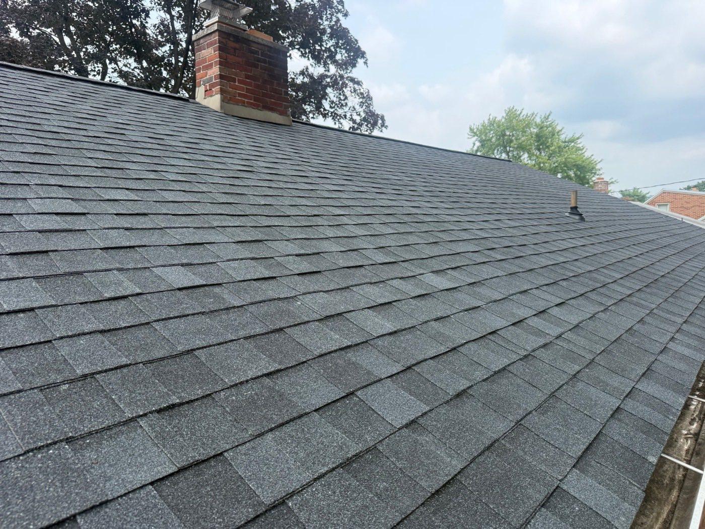 Close-up of new charcoal architectural shingles installed around a brick chimney