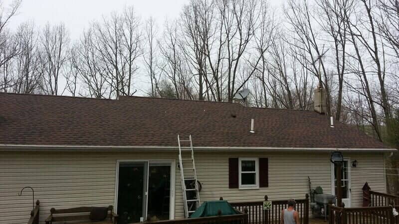 Rear of a ranch home with new shingle roof and a ladder up against the back