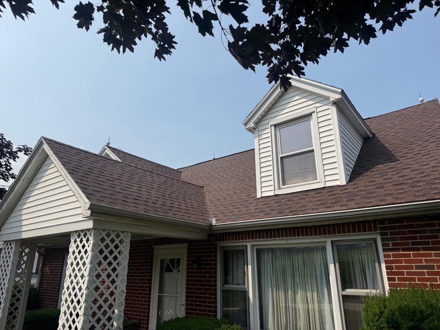 Brick and white-sided Cape Cod home with a dormer and a new brown architectural shingle roof