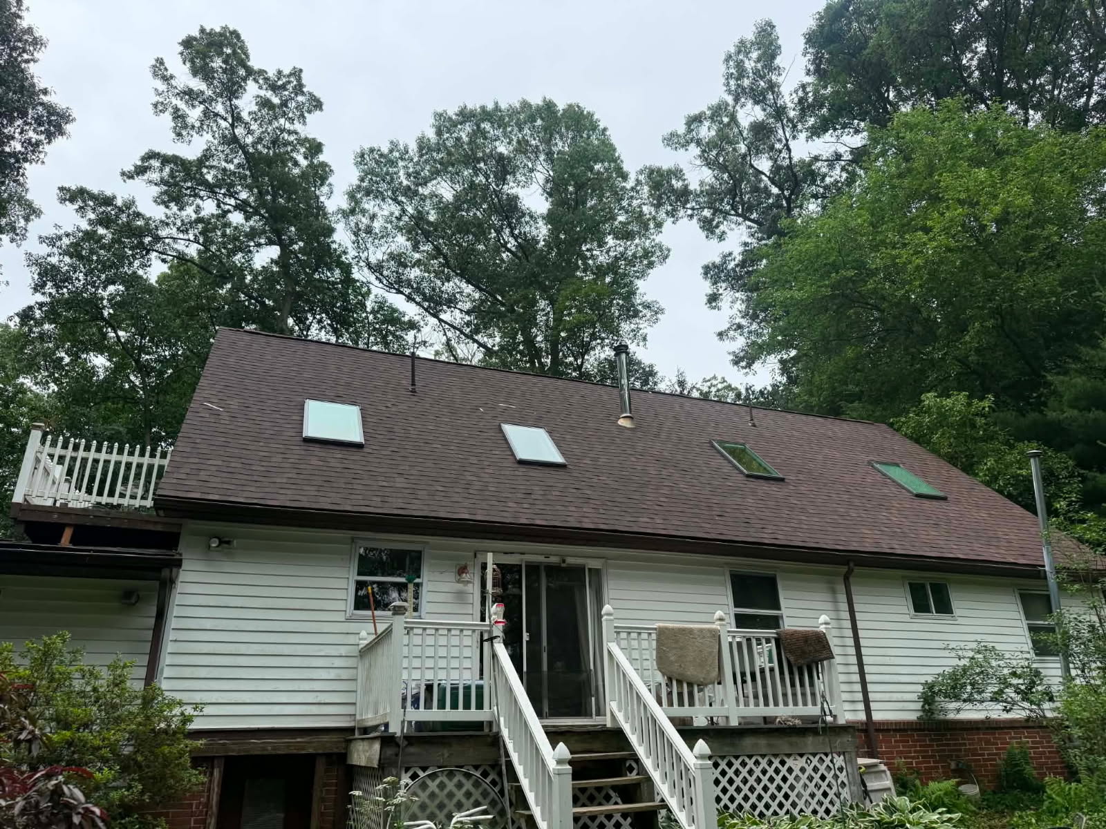 Rear of a Cape Cod home with a new brown architectural shingle roof, skylights, and a deck