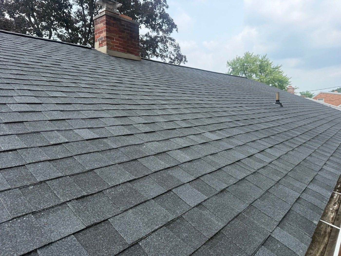 Close-up of new charcoal architectural shingles installed around a brick chimney