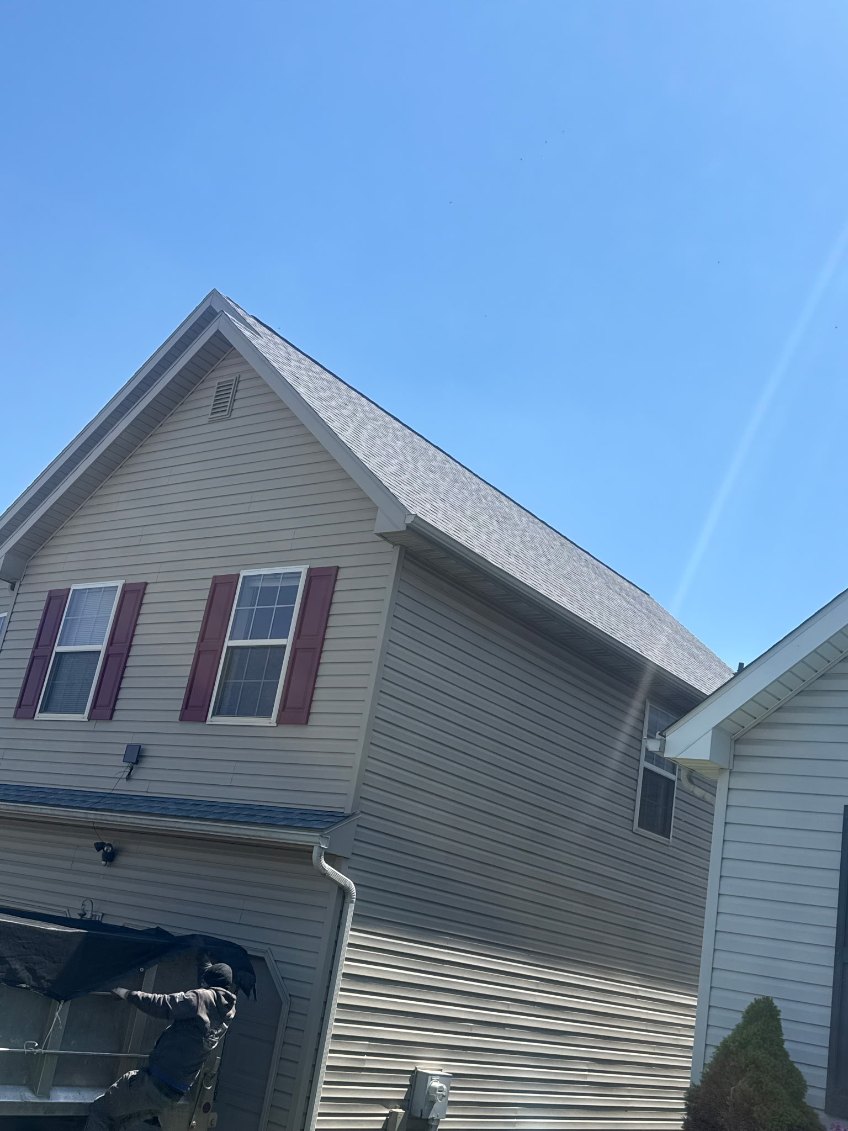 Dallastown crew member working on a shingle install on a tan-sided two-story home
