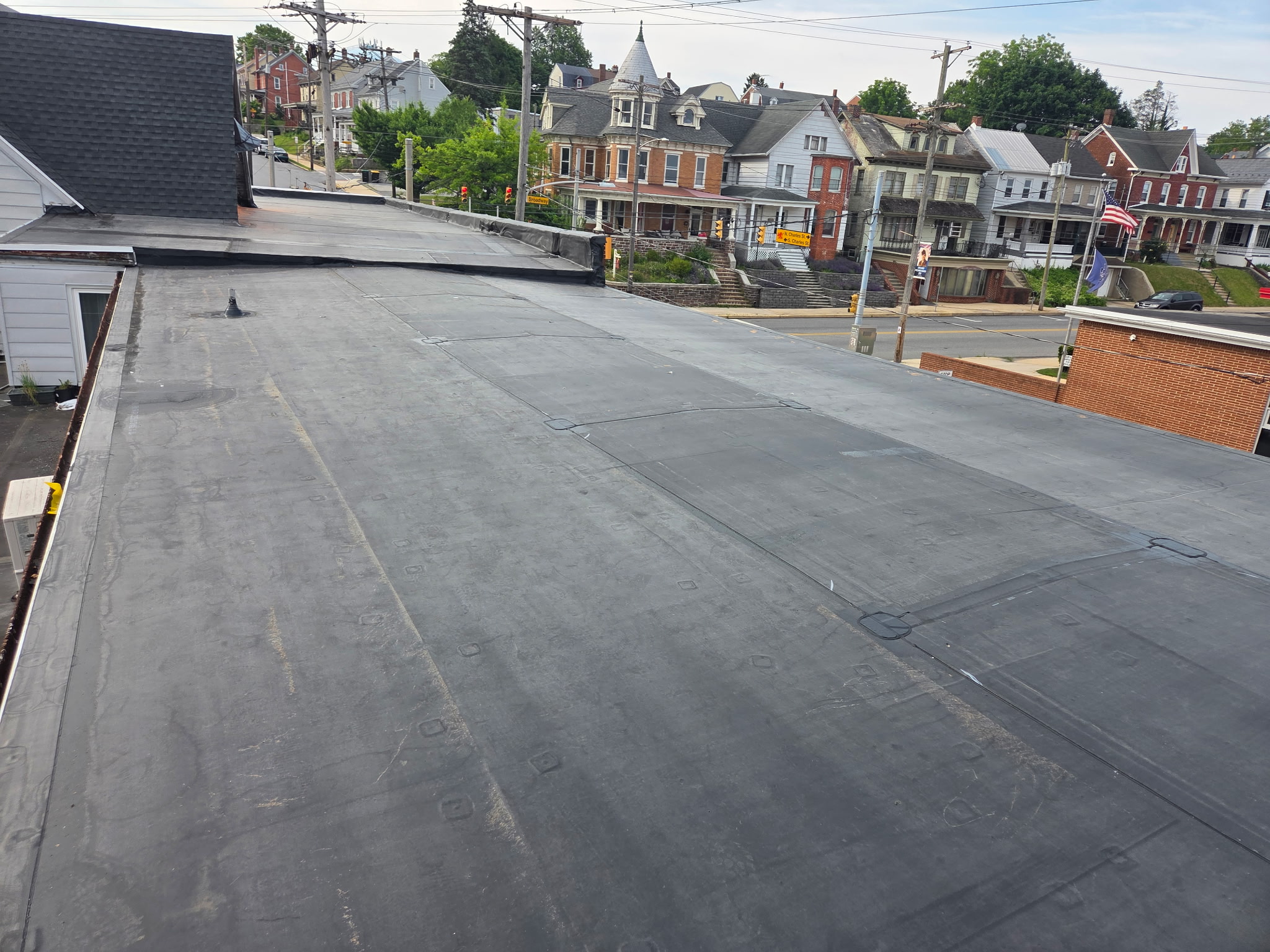 Freshly installed flat rubber roof with clean edge flashing above a residential street corner in York County