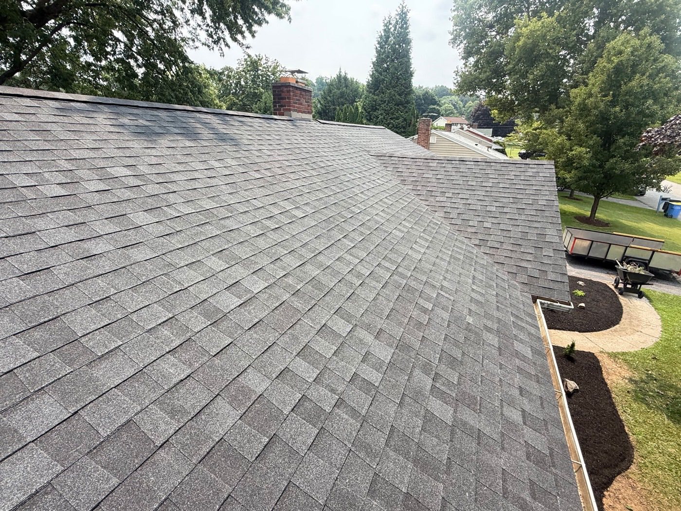 Aerial view of a freshly installed grey architectural shingle roof with a brick chimney