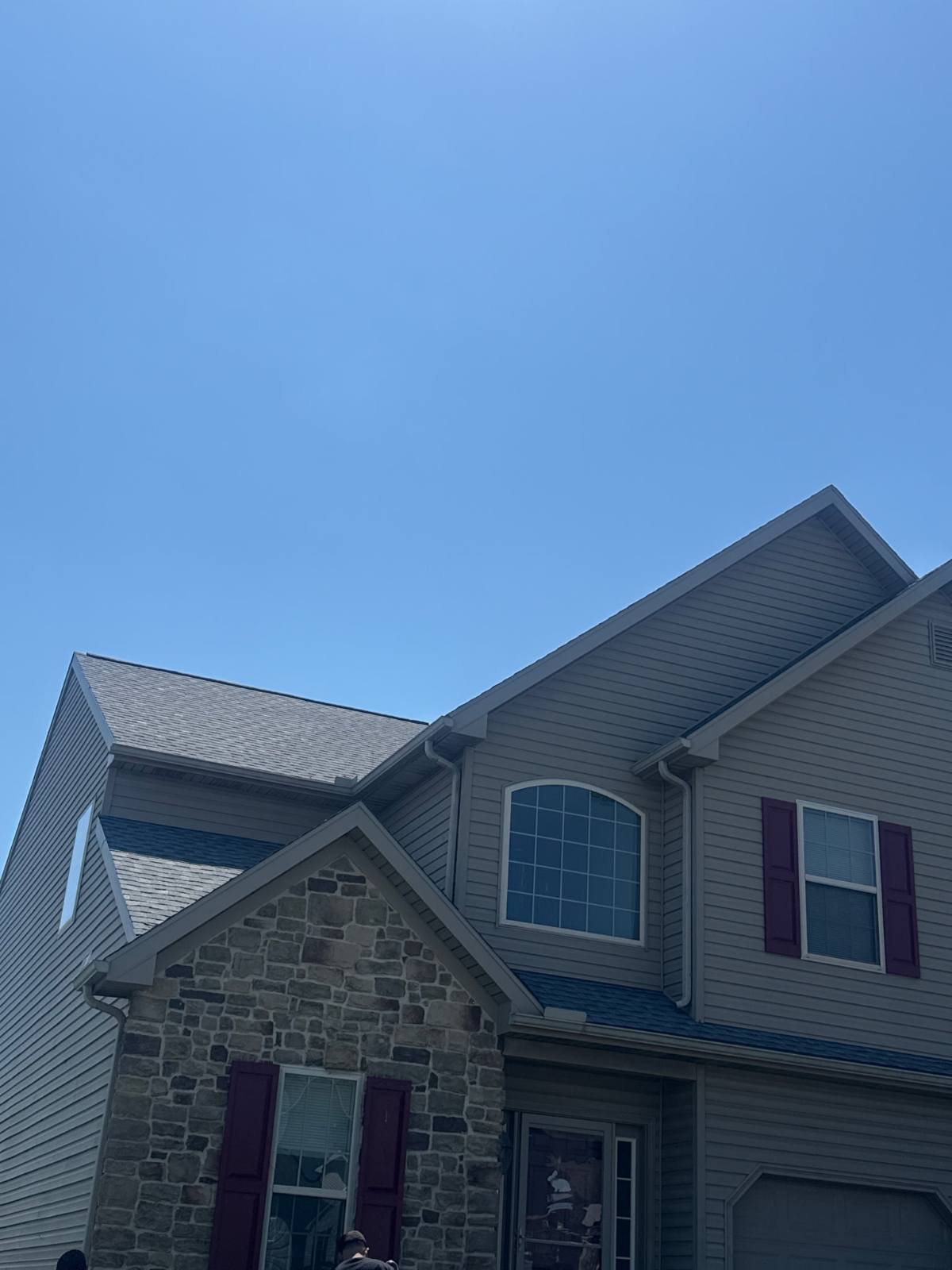 Two-story stone and vinyl-sided home with a new grey architectural shingle roof against a blue sky